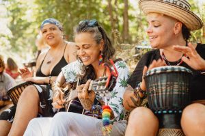 Women laughing and drumming together while one plays guitar